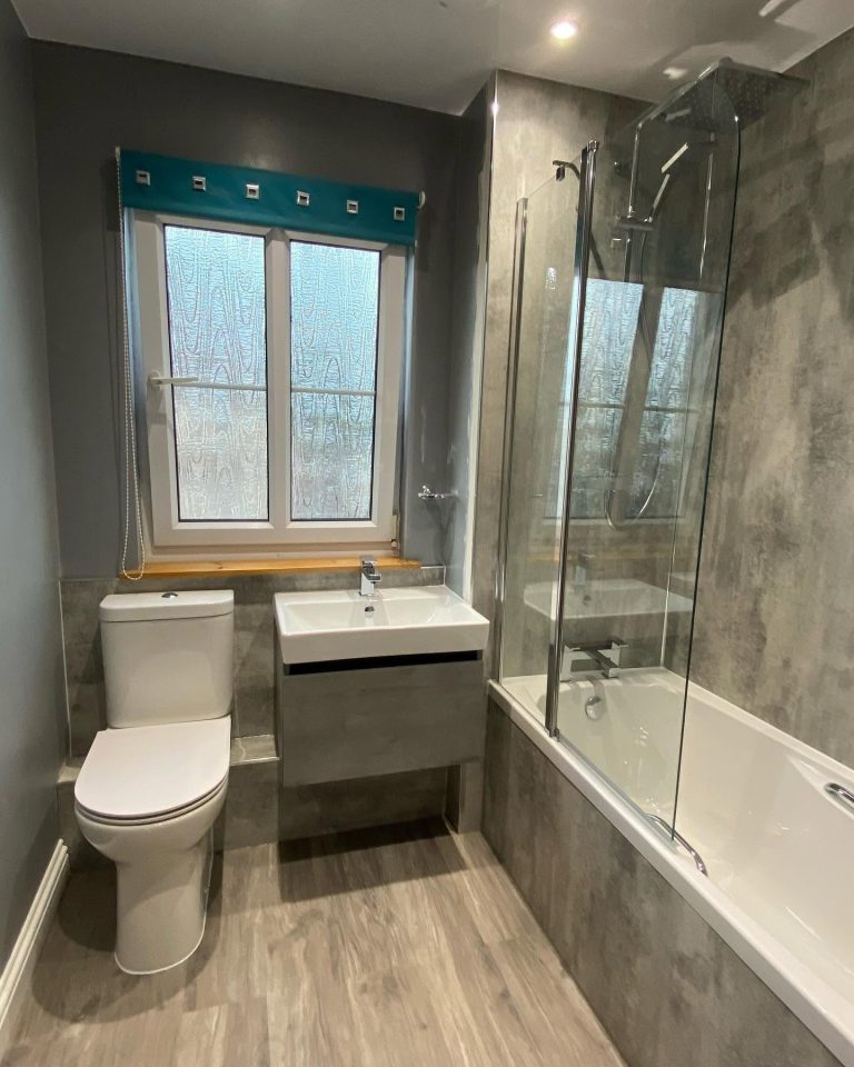 Compact modern bathroom featuring a bath with shower screen, contemporary vanity unit and elegant grey wall tiles.